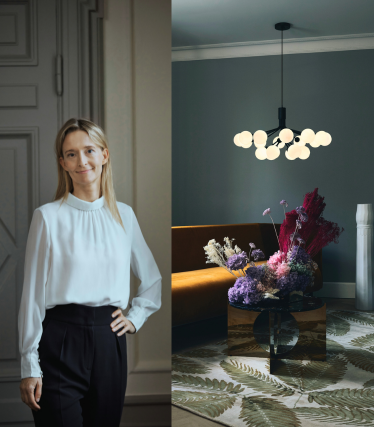 Porträt der Designerin Sofie Refer neben einer leuchtenden Pendelleuchte von Nuura in einem stilvollen Interior mit floralen Akzenten.