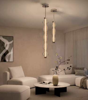 Zwei schlanke Glas-Pendelleuchten über einem Marmor-Couchtisch in einem hellen Wohnzimmer mit weißem Sofa und Sessel.
