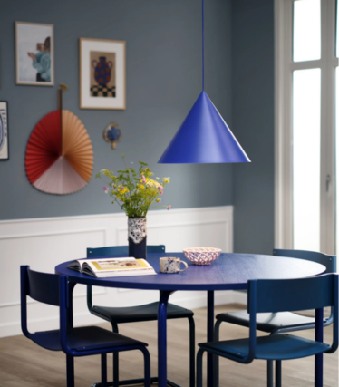 Blaue kegelförmige Pendelleuchte über rundem blauem Esstisch mit Blumenstrauß, in einem Esszimmer mit blauer Wand und Kunstwerken.