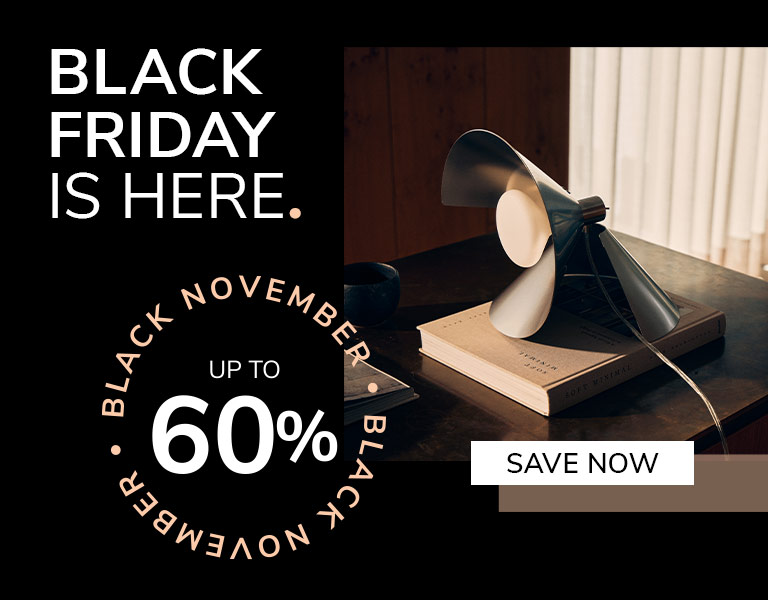 A modern table lamp with angled metal blades sits on top of a book on a dark wooden desk in soft daylight. Text reads: &lsquo;Black Friday is here. Up to 60%. Save Now.