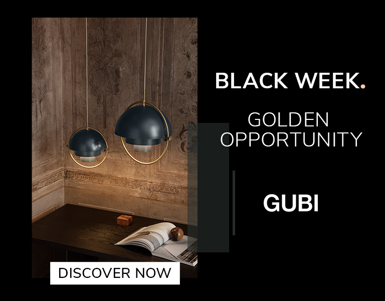 Two modern pendant lamps with dark blue domes and gold accents hanging above a wooden desk in a warmly lit, ornate room. Text reads: &lsquo;Black Week. Golden Opportunity. GUBI.&rsquo; A button says &lsquo;Discover Now.